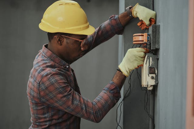 Person wearing a hard hat, glasses, and gloves checking wires